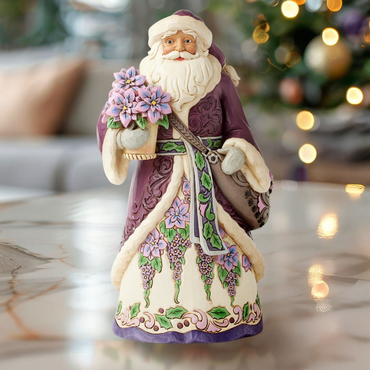 The stunning purple Santa representing Jim Shores trademark colour. Radiating elegance in rich purples, plums, and greens, carrying a vibrant purple poinsettias. His intricately detailed cloak features delicate rosemaling, while his robes bloom with festivities.