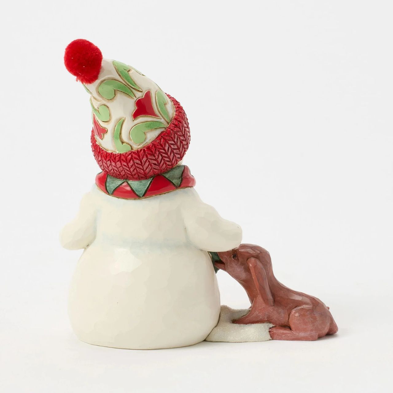 This charming Jim Shore pint snowman brings holiday joy with a playful scene of a curious puppy tugging at his scarf. Wearing a vibrant floral knit cap, the snowman smiles warmly, capturing the spirit of fun and friendship in wintertime.