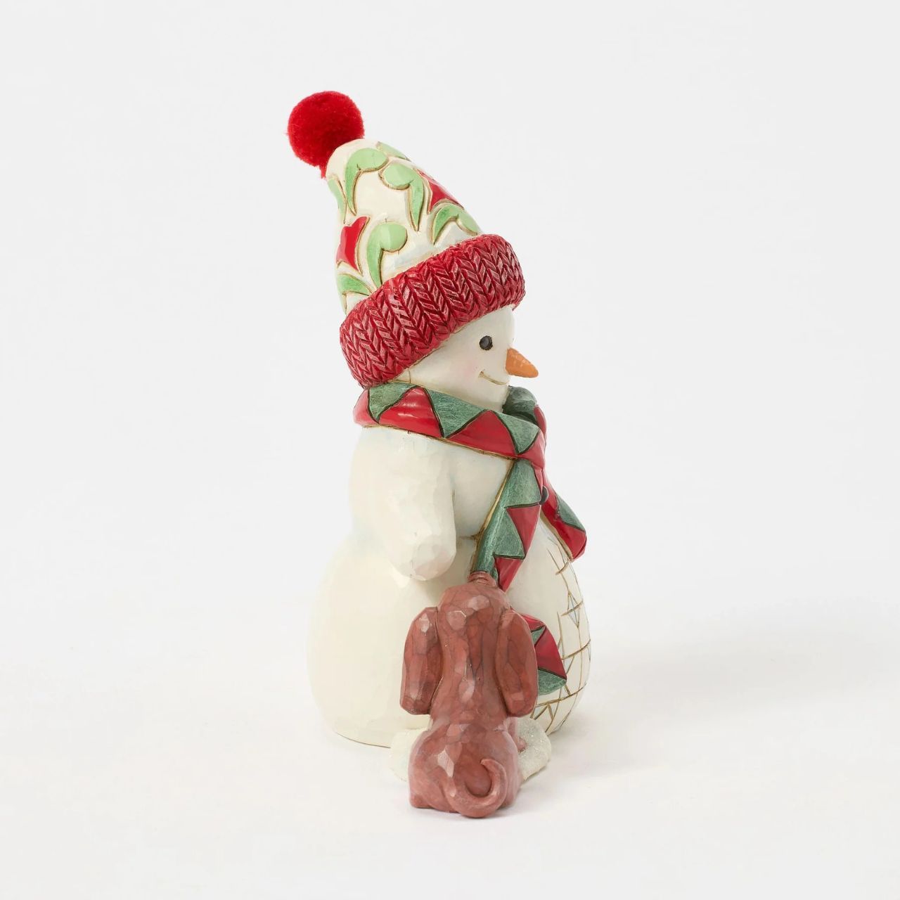 This charming Jim Shore pint snowman brings holiday joy with a playful scene of a curious puppy tugging at his scarf. Wearing a vibrant floral knit cap, the snowman smiles warmly, capturing the spirit of fun and friendship in wintertime.