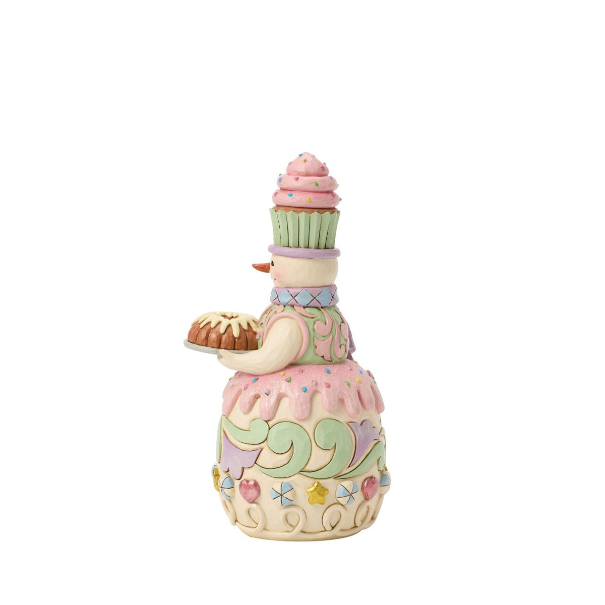 This charming gingerbread snowman proudly carries a frosted bunt cake, ready for holiday feasts. Jim Shore's folk patterns blend with candy-sweet colours, making him as warm and inviting as fresh-baked treats.
