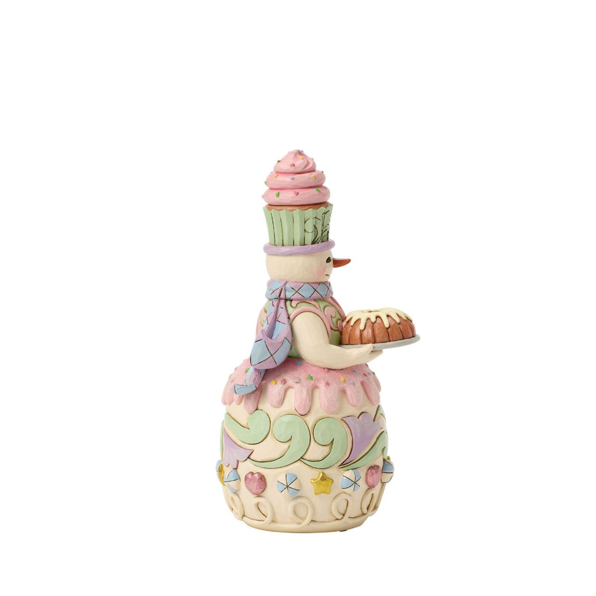 This charming gingerbread snowman proudly carries a frosted bunt cake, ready for holiday feasts. Jim Shore's folk patterns blend with candy-sweet colours, making him as warm and inviting as fresh-baked treats.