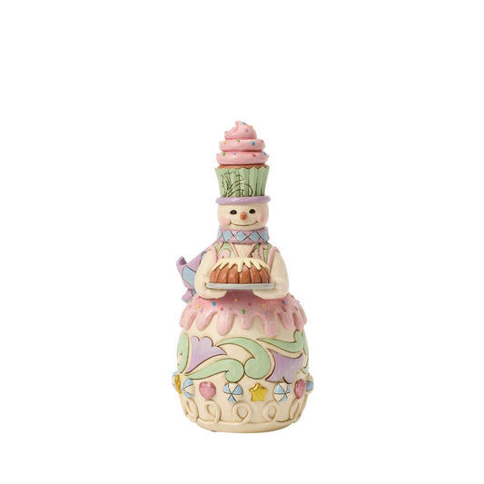This charming gingerbread snowman proudly carries a frosted bunt cake, ready for holiday feasts. Jim Shore's folk patterns blend with candy-sweet colours, making him as warm and inviting as fresh-baked treats.
