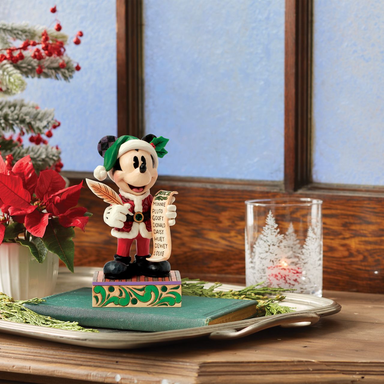 In this enchanting Jim Shore Christmas scene, Mickey Mouse dons a striking red rosemaling suit accented with a green jewelled belt and a Santa hat trimmed with holly. He holds a quill and a list of Naughty and Nice Disney characters with a smile.