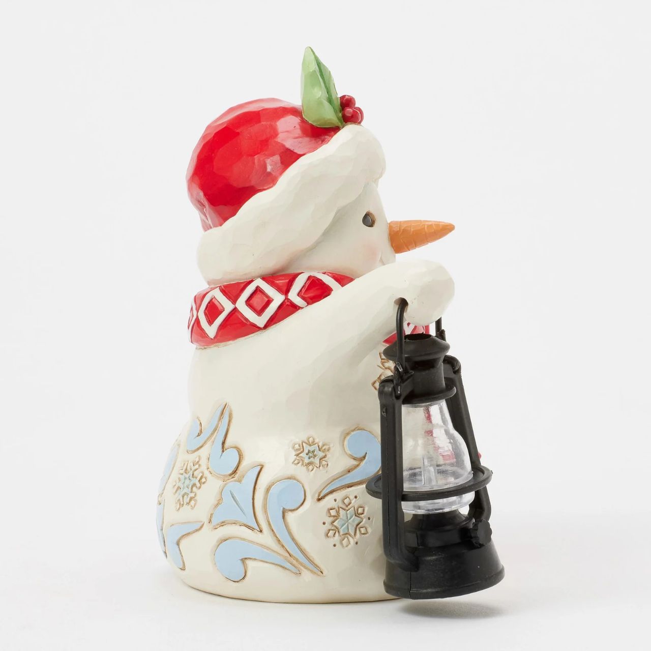 This delightful Jim Shore pint snowman carries a glowing candlelit lantern, spreading warmth and light. Dressed in a Santa hat adorned with holly, a patterned scarf, and snowflake accents, his rosy cheeks and bright smile spread Christmas cheer.