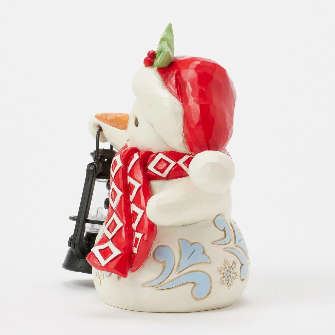 This delightful Jim Shore pint snowman carries a glowing candlelit lantern, spreading warmth and light. Dressed in a Santa hat adorned with holly, a patterned scarf, and snowflake accents, his rosy cheeks and bright smile spread Christmas cheer.