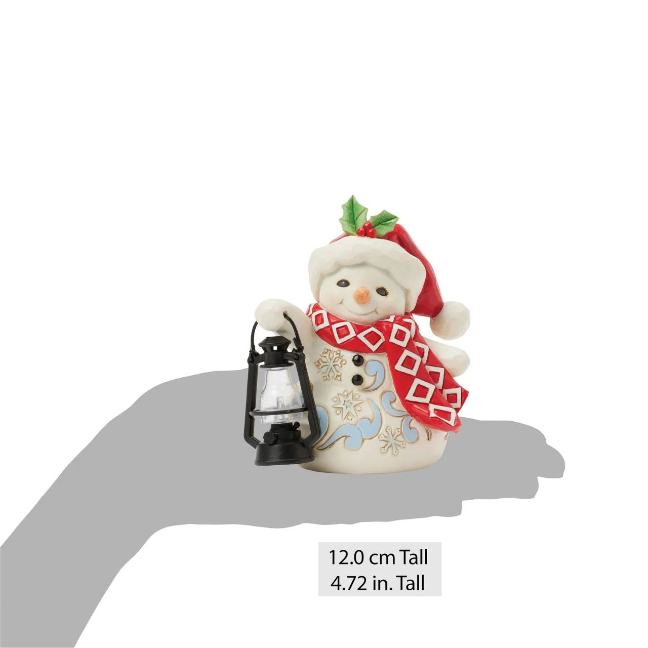 This delightful Jim Shore pint snowman carries a glowing candlelit lantern, spreading warmth and light. Dressed in a Santa hat adorned with holly, a patterned scarf, and snowflake accents, his rosy cheeks and bright smile spread Christmas cheer.