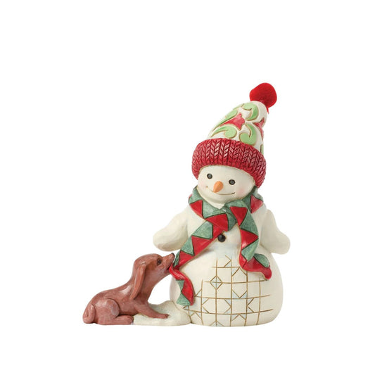 This charming Jim Shore pint snowman brings holiday joy with a playful scene of a curious puppy tugging at his scarf. Wearing a vibrant floral knit cap, the snowman smiles warmly, capturing the spirit of fun and friendship in wintertime.