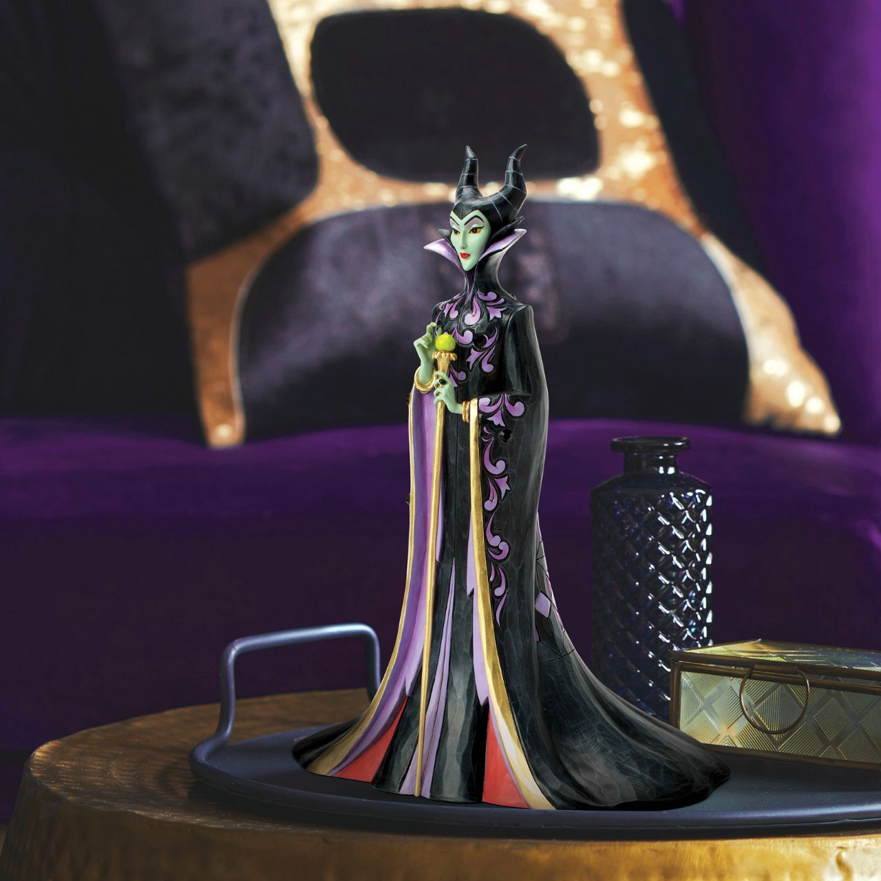 This Jim Shore design captures the vengeful villainess, Maleficent, in her striking black and purple cloak adorned with Shore's quilt and rosemaling patterns. With a sinister gaze, she taps her staff, channeling dark magic with malice in her heart.