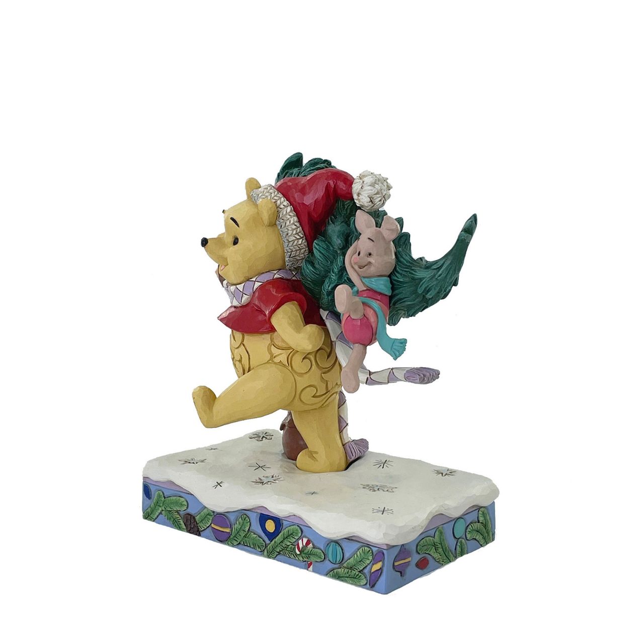 In this delightful Jim Shore scene, Winnie the Pooh sports intricate rosemaling and a Santa hat adorned with holly as he joyfully carries home a Christmas tree with Piglet in tow. They march through the snow on a festive stage of ornaments.