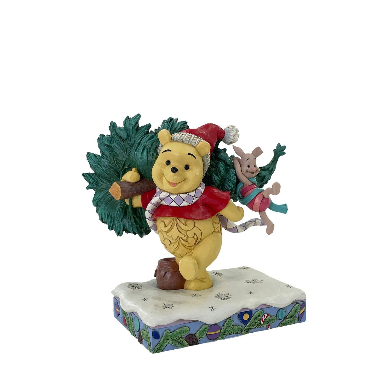 In this delightful Jim Shore scene, Winnie the Pooh sports intricate rosemaling and a Santa hat adorned with holly as he joyfully carries home a Christmas tree with Piglet in tow. They march through the snow on a festive stage of ornaments.