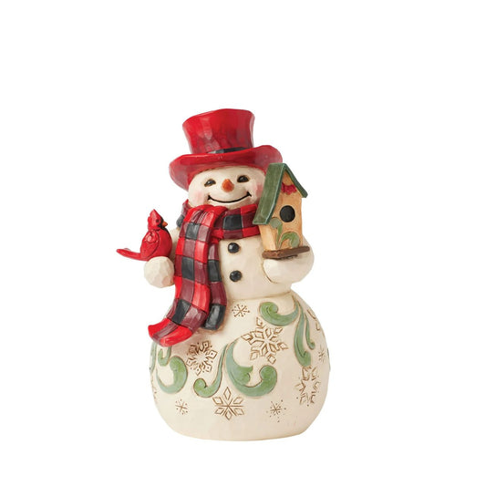 This whimsical Jim Shore Highland Glen snowman wears a cozy buffalo plaid scarf and a vibrant red top hat. Holding a charming birdhouse with a friendly cardinal perched beside him, his joyful smile radiates warmth and holiday spirit.