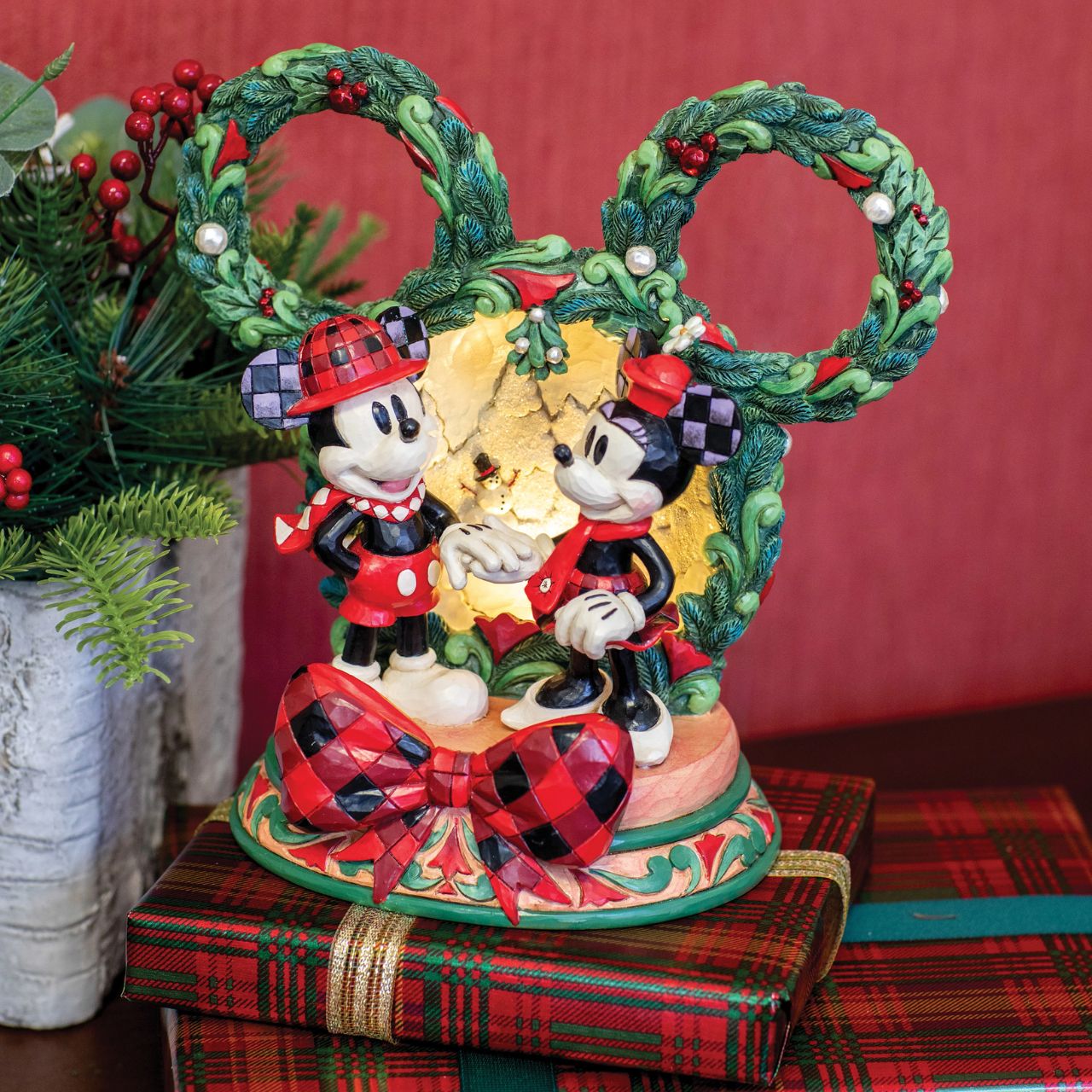 This delightful Jim Shore Christmas scene captures Mickey and Minnie holding hands beneath a glowing LED diorama, framed by a festive Mickey-shaped garland adorned with berries and pearl accents. It radiates seasonal magic with holiday charm.