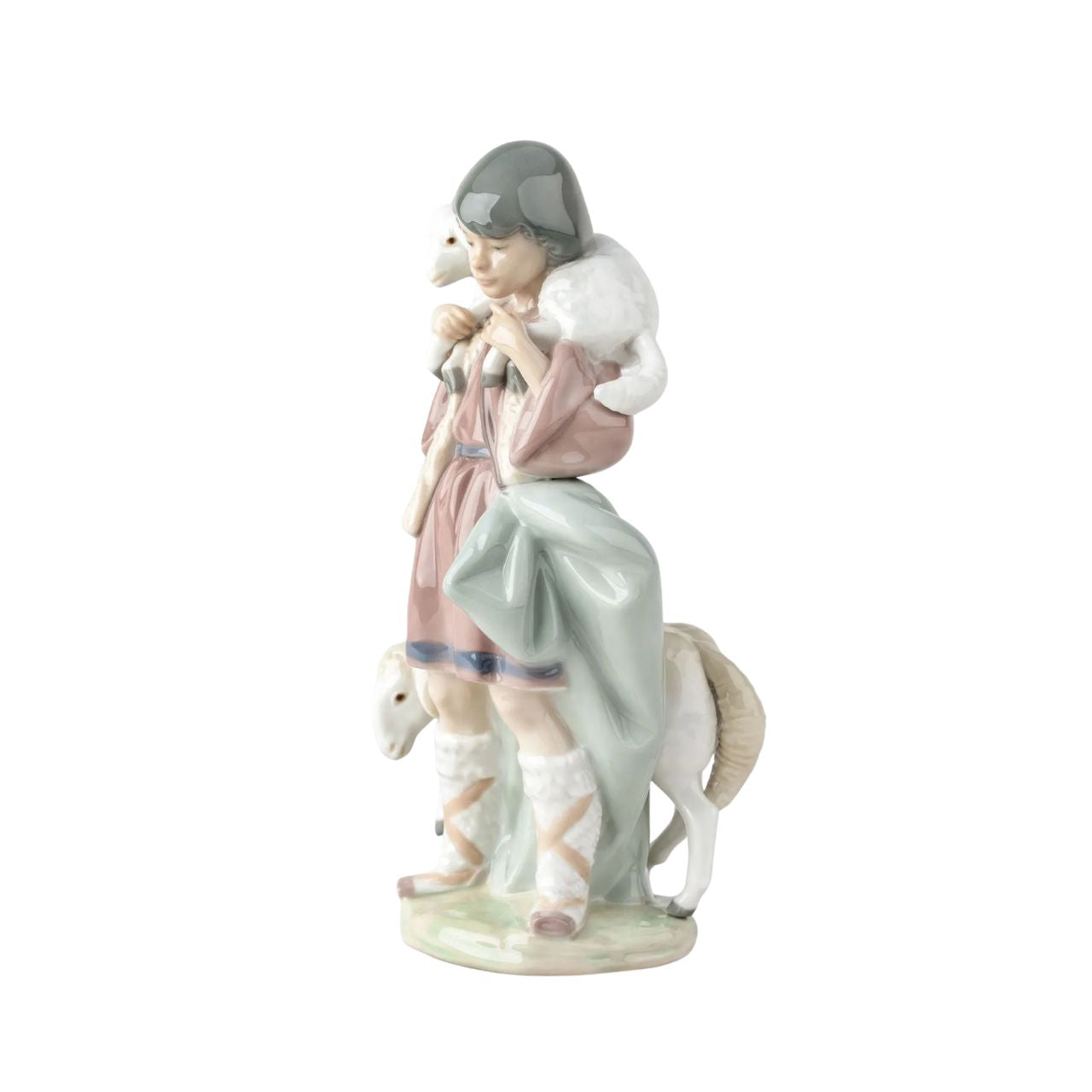 A young shepherd comes to worship the newborn Child Jesus, with a lamb on his shoulders and another close to his legs. It is part of a group of pieces that form a complete Nativity scene, the most important scene for all Christians in the world. It is a glossy porcelain piece decorated with Lladró's classic pastel color palette, a set designed to create a warm and welcoming atmosphere in the home during the family days of Christmas.