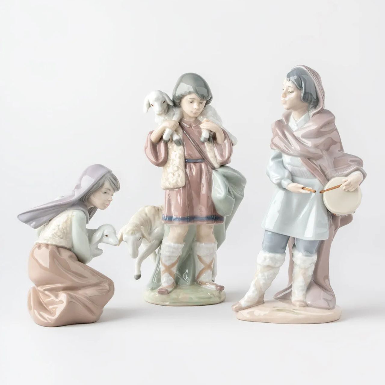 A young shepherd comes to worship the newborn Child Jesus, with a lamb on his shoulders and another close to his legs. It is part of a group of pieces that form a complete Nativity scene, the most important scene for all Christians in the world. It is a glossy porcelain piece decorated with Lladró's classic pastel color palette, a set designed to create a warm and welcoming atmosphere in the home during the family days of Christmas.