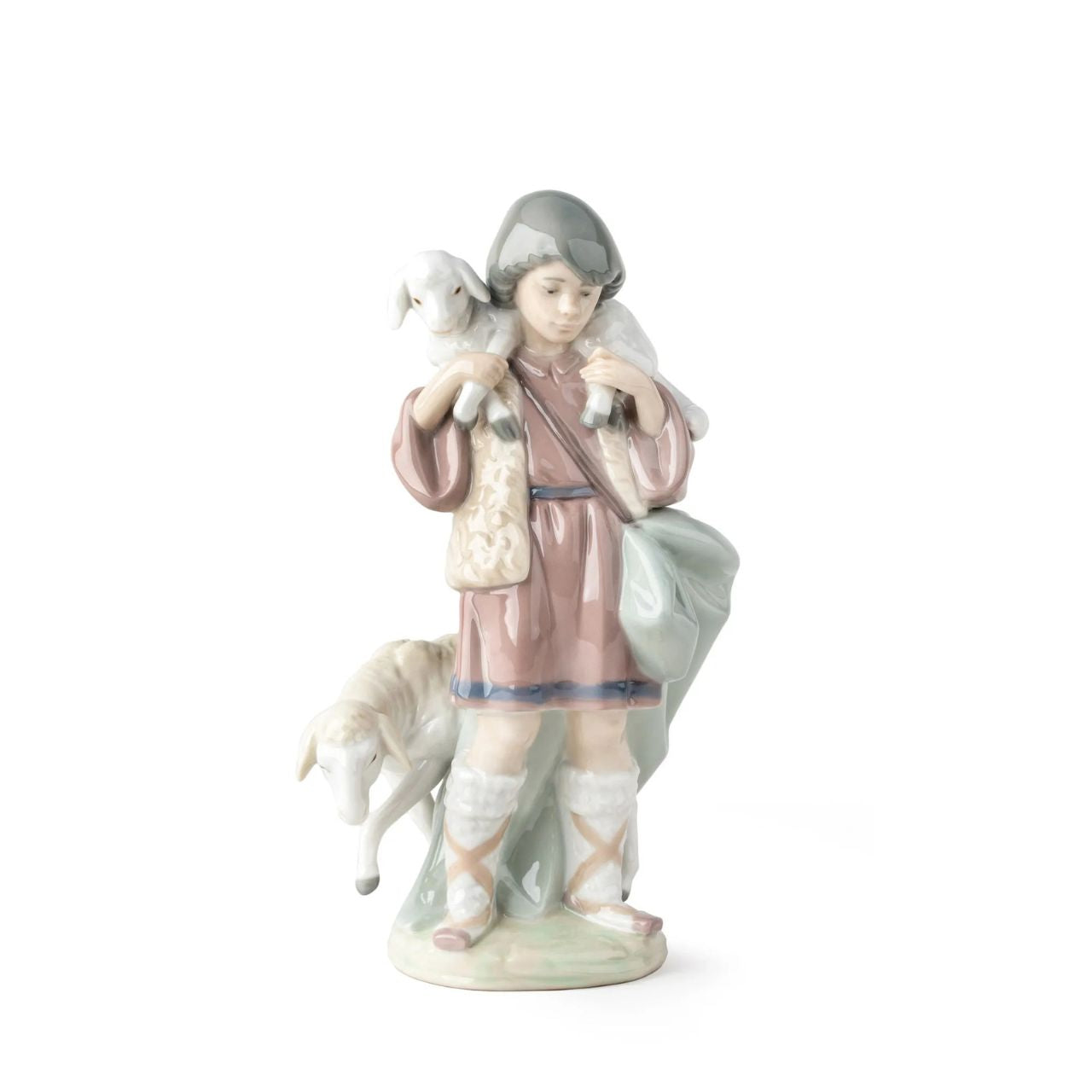 A young shepherd comes to worship the newborn Child Jesus, with a lamb on his shoulders and another close to his legs. It is part of a group of pieces that form a complete Nativity scene, the most important scene for all Christians in the world. It is a glossy porcelain piece decorated with Lladró's classic pastel color palette, a set designed to create a warm and welcoming atmosphere in the home during the family days of Christmas.