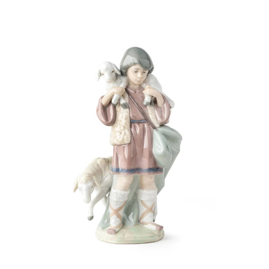 A young shepherd comes to worship the newborn Child Jesus, with a lamb on his shoulders and another close to his legs. It is part of a group of pieces that form a complete Nativity scene, the most important scene for all Christians in the world. It is a glossy porcelain piece decorated with Lladró's classic pastel color palette, a set designed to create a warm and welcoming atmosphere in the home during the family days of Christmas.