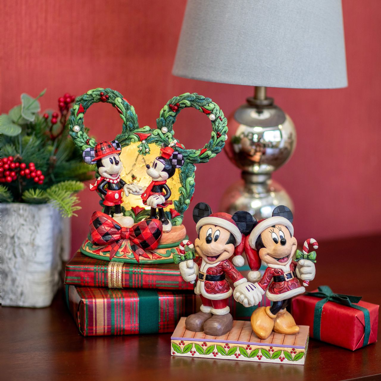 This delightful Jim Shore Christmas scene captures Mickey and Minnie holding hands beneath a glowing LED diorama, framed by a festive Mickey-shaped garland adorned with berries and pearl accents. It radiates seasonal magic with holiday charm.