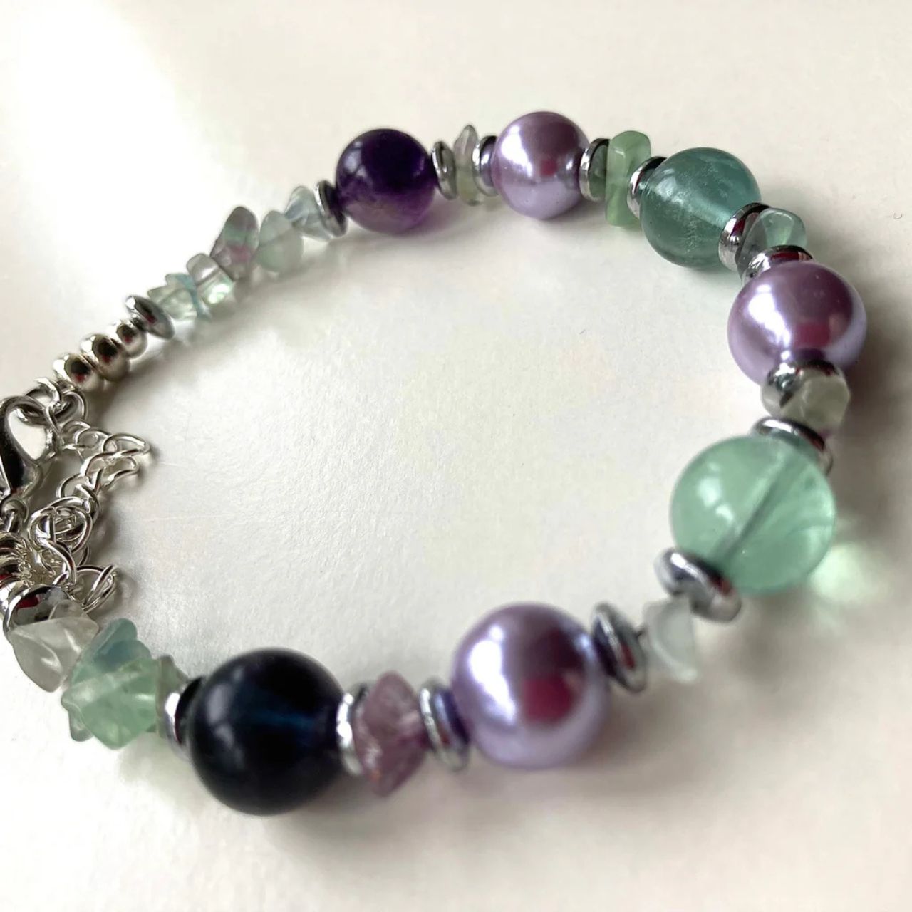 In this bracelet we have green and purple Flourite gemstone chips and round beads combined with lilac Glass Pearls and silver plated Hematite gemstone rondelles.