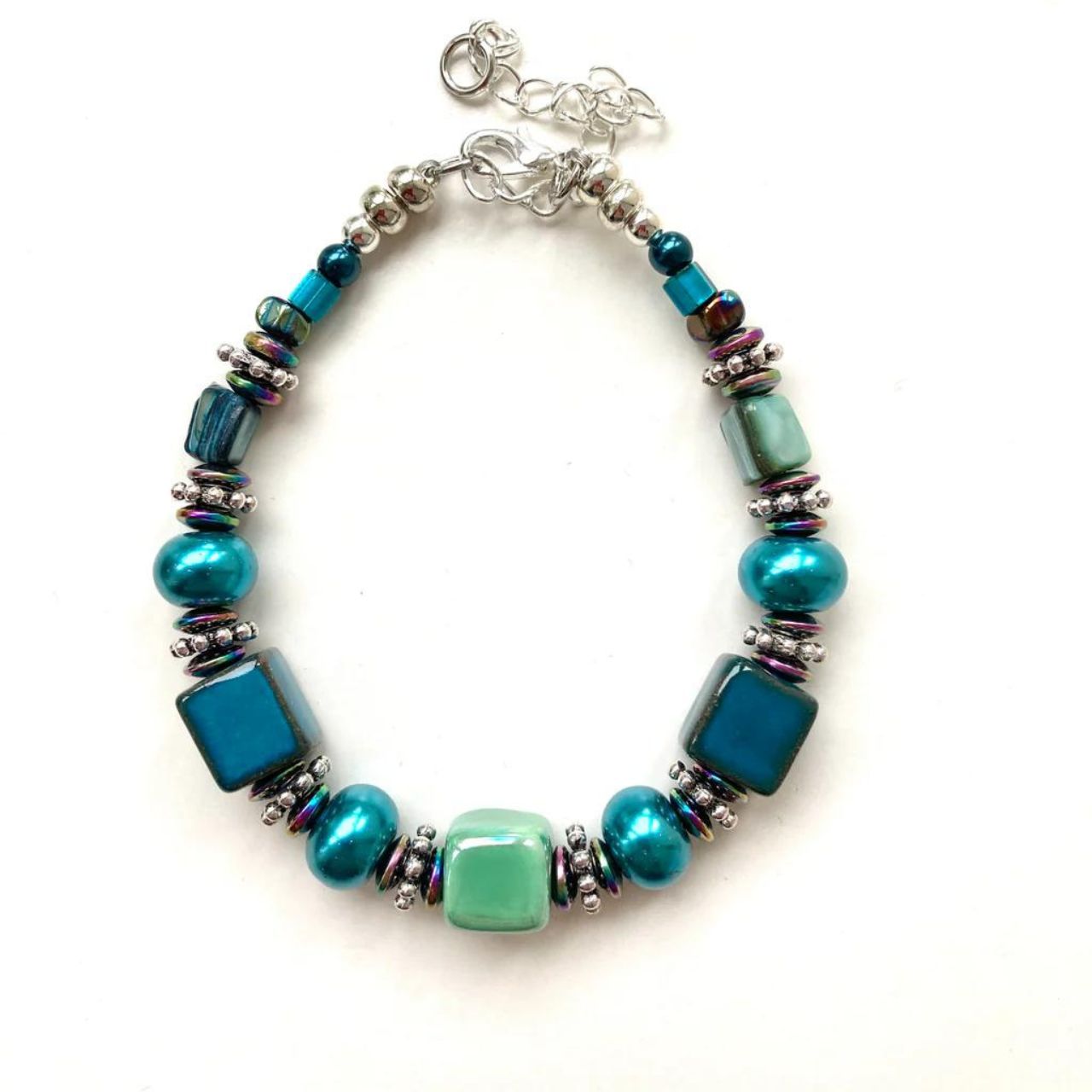 This bracelet features handmade Ceramic cubes in seagreen and teal with Turquoise Pearl Rondelles, teal coloured Shell beads, tiny iridescent Hematite gemstone rondelles and decorative silver-toned elements.