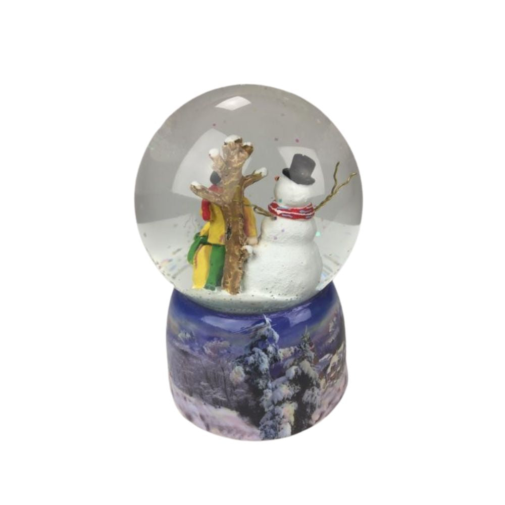 Musicbox World Snow Globe Snowman & Dog  Snow globe with snowman. In the ball filled with glitter and snow, a man stands with his dog and looks at the tall smiling snowman standing close to a tree. The base is painted with a snowy wintery village landscape. By winding up the mechanical movement with the disc, the music box turns on the disc to the melody “Silent Night”. 