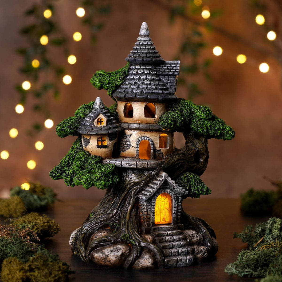 The Mystic Legends LED Treehouse 20cm is an enchanting decorative piece, designed to capture the magic of a hidden woodland dwelling. The ornament features a beautifully detailed miniature house built into a gnarled tree trunk, complete with textured bark, layered stonework, and lush green foliage that wraps around the structure.