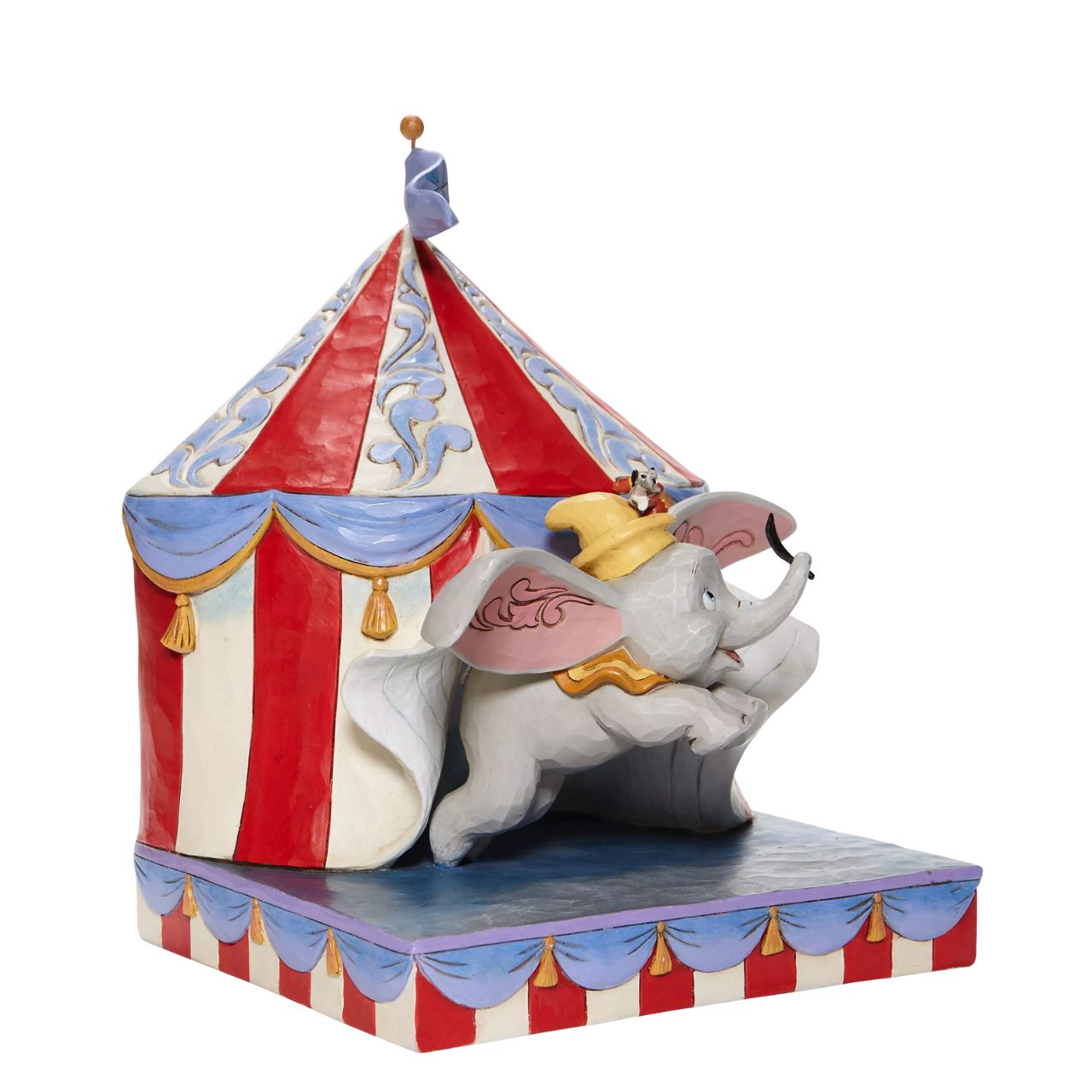 Jim Shore Over the Big Top - Dumbo Circus out of Tent Figurine  With Timothy's encouragement, guidance, and the willingness from a feather, Dumbo takes his favourite friend on an adventurous flight. This Disney piece by Jim Shore is intricately hand-painted and detailed with folk art motifs and is great for any Dumbo fan.