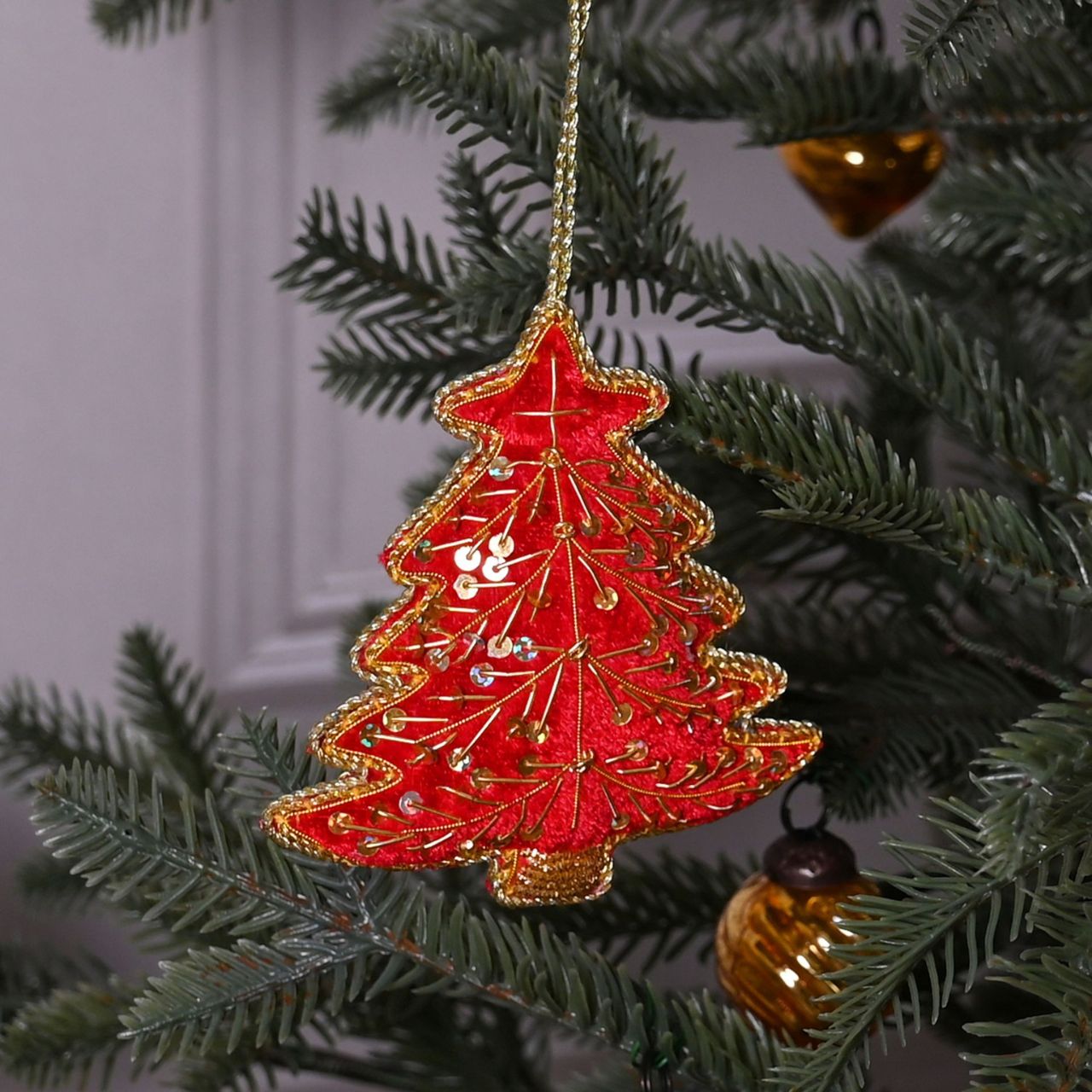 The padded velvet, tree shaped decoration showcases a striking red &amp; gold finish which complements the matching sequin embellishments and gold edging. It hangs from the tree using the attached gold string hanger.