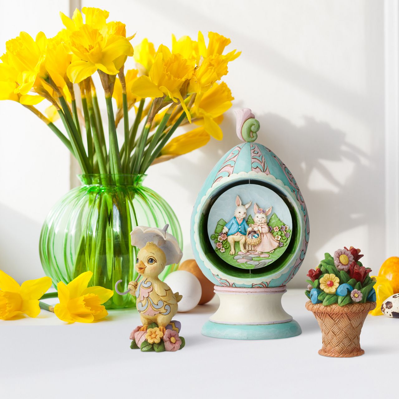 Revolving Egg with Bunnies and Chicks Scene Figurine by Jim Shore  Stroll through Spring with this festive Jim Shore tabletop Easter egg. Simply turn the floral finial atop the egg to rotate the scene inside between two adorable Easter scenes. Chicks soak in the sun while a pair of bunnies jubilantly collect eggs.