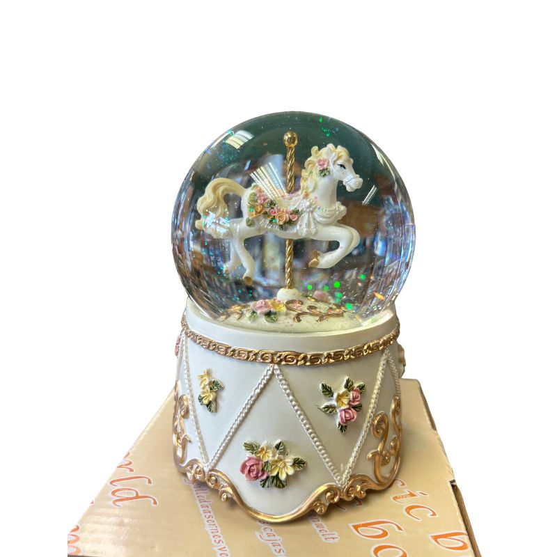 Glitter globe with carousel horse. The decorated carousel horse stands on a gold-coloured pole in the globe filled with glitter. The floor and the base are decorated with flowers, tendrils and ornaments. Shiny stones are attached to the base.