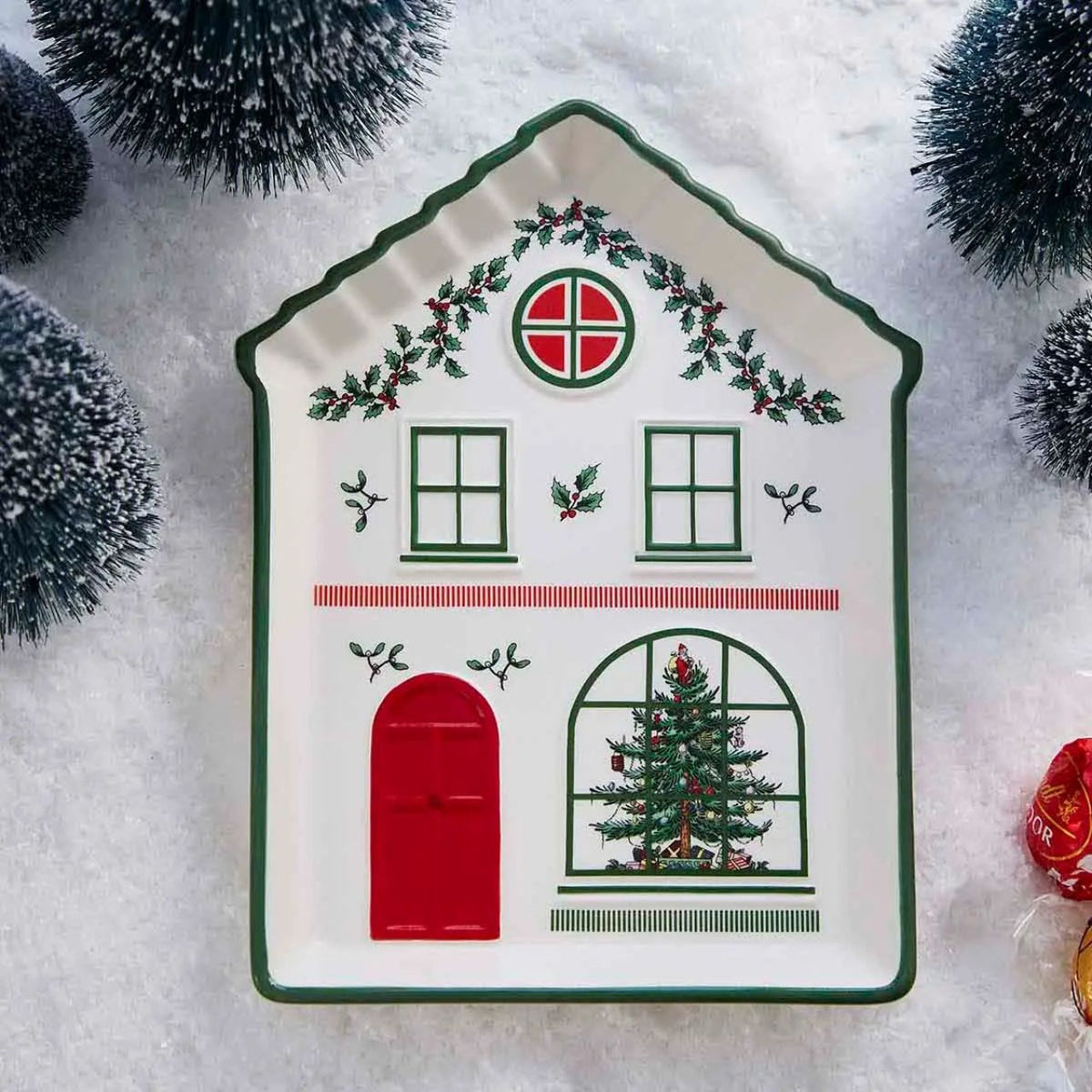 This charming ceramic tidbit tray from Spode is shaped like the front of a delightfully festive house, perfect for adding a touch of holiday charm to your table. The house features a welcoming green door flanked by two charming Christmas trees, inviting red windows, and a delightful display of festive foliage.