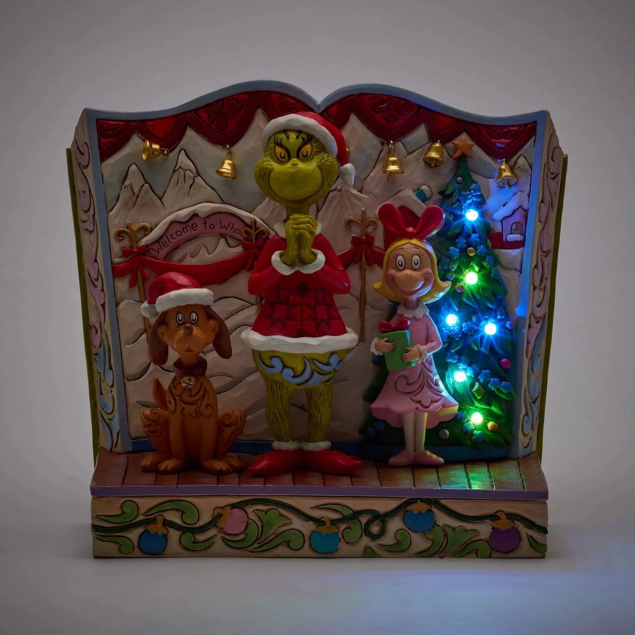 Framed within the classic Dr. Seuss book, this Jim Shore piece captures The Grinch's heartwarming transformation with Cindy Lou and Max by his side. Dressed as Santa, he smiles with rosemaling, patchwork patterns, and real jingle bell details.