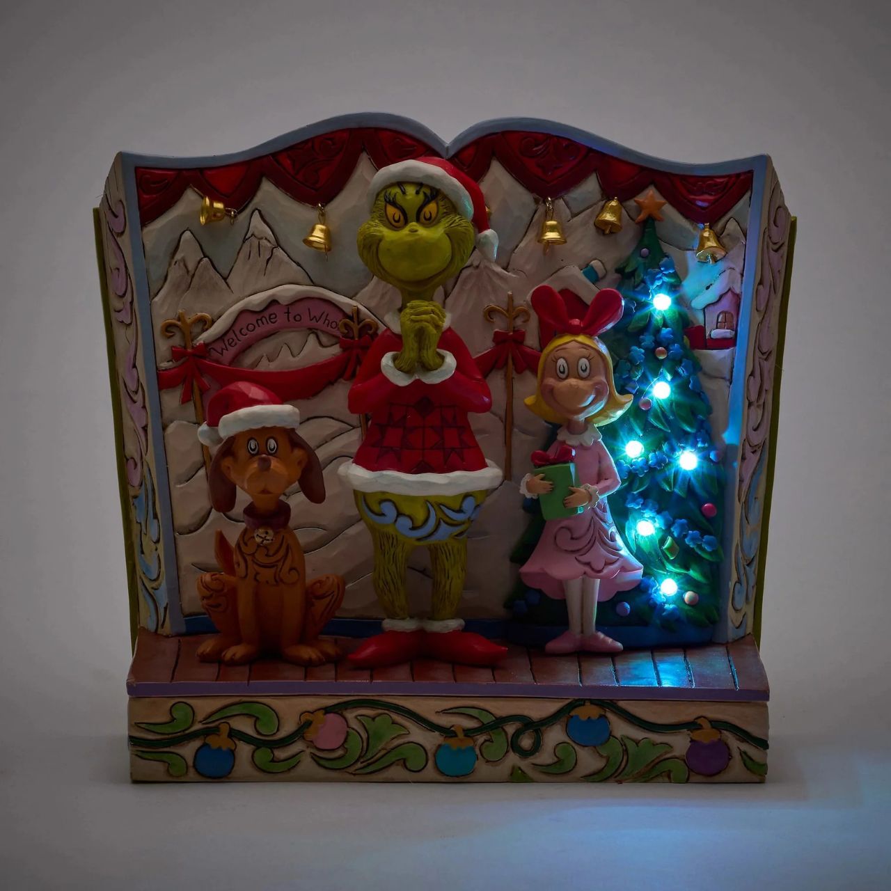 Framed within the classic Dr. Seuss book, this Jim Shore piece captures The Grinch's heartwarming transformation with Cindy Lou and Max by his side. Dressed as Santa, he smiles with rosemaling, patchwork patterns, and real jingle bell details.