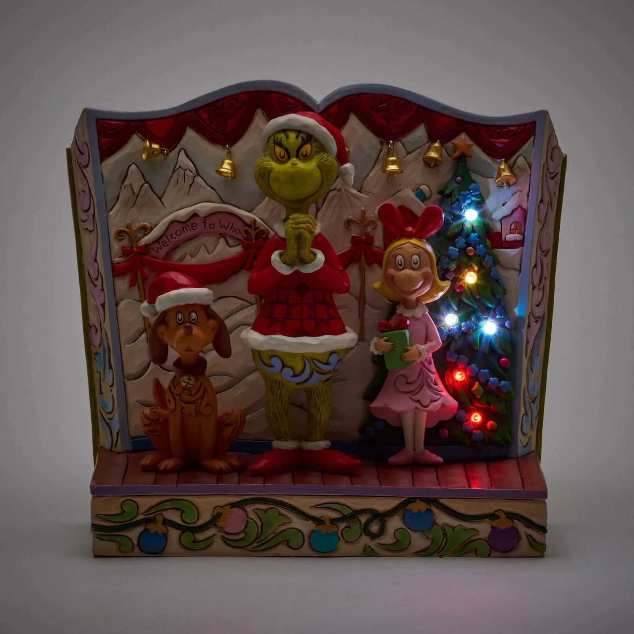 Framed within the classic Dr. Seuss book, this Jim Shore piece captures The Grinch's heartwarming transformation with Cindy Lou and Max by his side. Dressed as Santa, he smiles with rosemaling, patchwork patterns, and real jingle bell details.