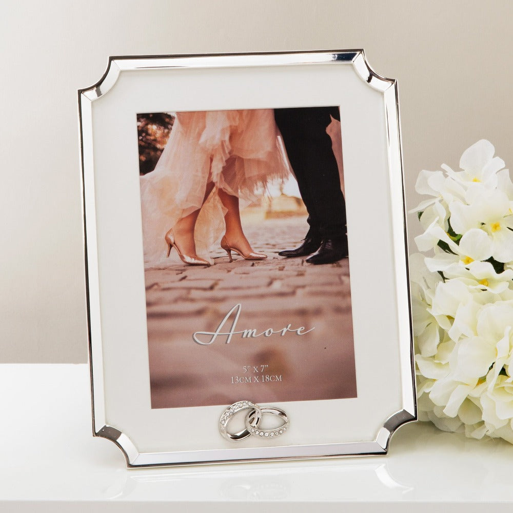 AMORE BY JULIANA® Silver Scalloped Corner Frame 5" x 7"  A beautiful silver plated cut corner 5" x 7" (13x18cm) photo frame. The frame features an intertwined silverplated crystal ring icon, a crisp white mount and a standing strut.