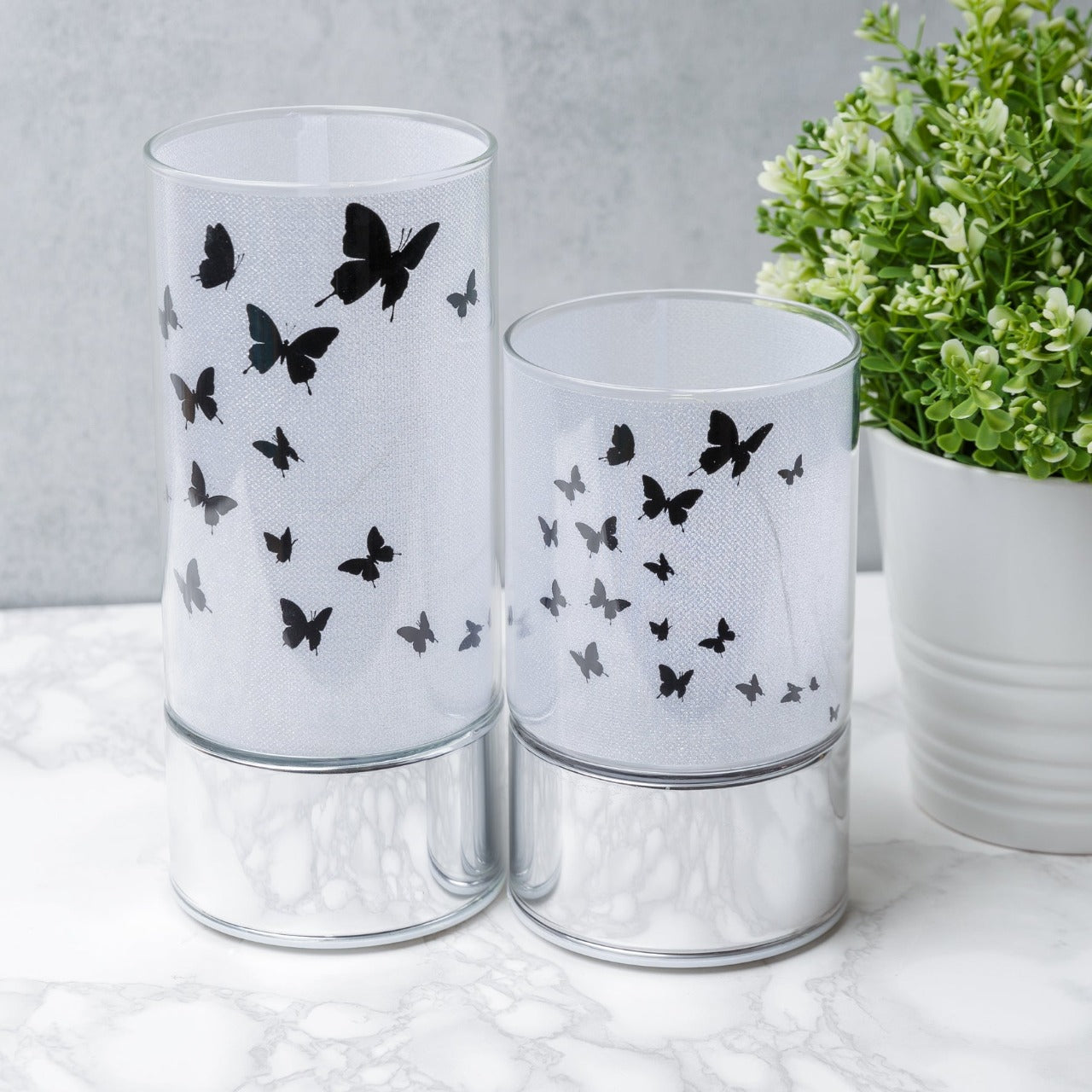 HESTIA® Glass Butterfly Design Tube with LED Lights 15cm  A beautiful LED tube from HESTIA®'s Silver Luxe collection. Featuring a dazzling glitter finish with butterfly design on a metal base. Requires 3 x AA batteries for use.