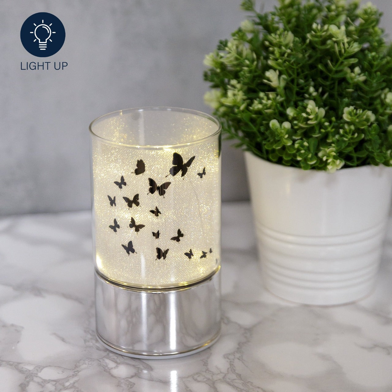 HESTIA® Glass Butterfly Design Tube with LED Lights 15cm  A beautiful LED tube from HESTIA®'s Silver Luxe collection. Featuring a dazzling glitter finish with butterfly design on a metal base. Requires 3 x AA batteries for use.