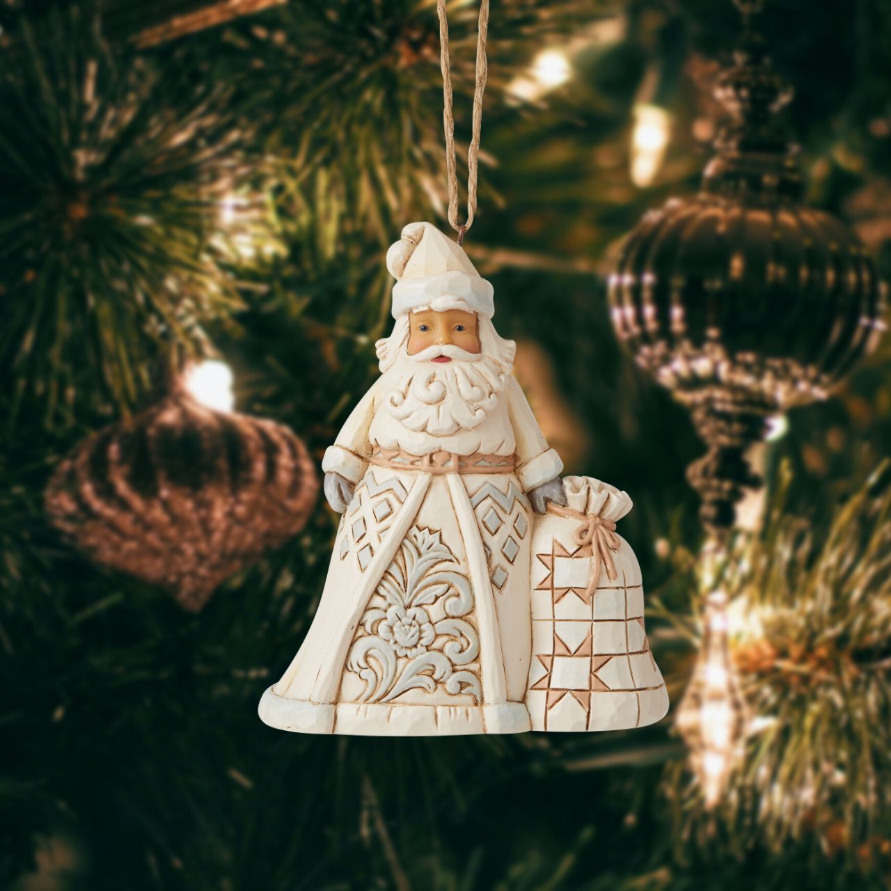 Jim Shore Heartwood Creek White Woodland Santa Hanging Ornament  In muted colors, this cool hued Santa brings grandeur with his deliveries. With a bag heavy with presents, this Christmas hero smiles happily from your tree, admiring the nice boys and girls as they open presents in your home.