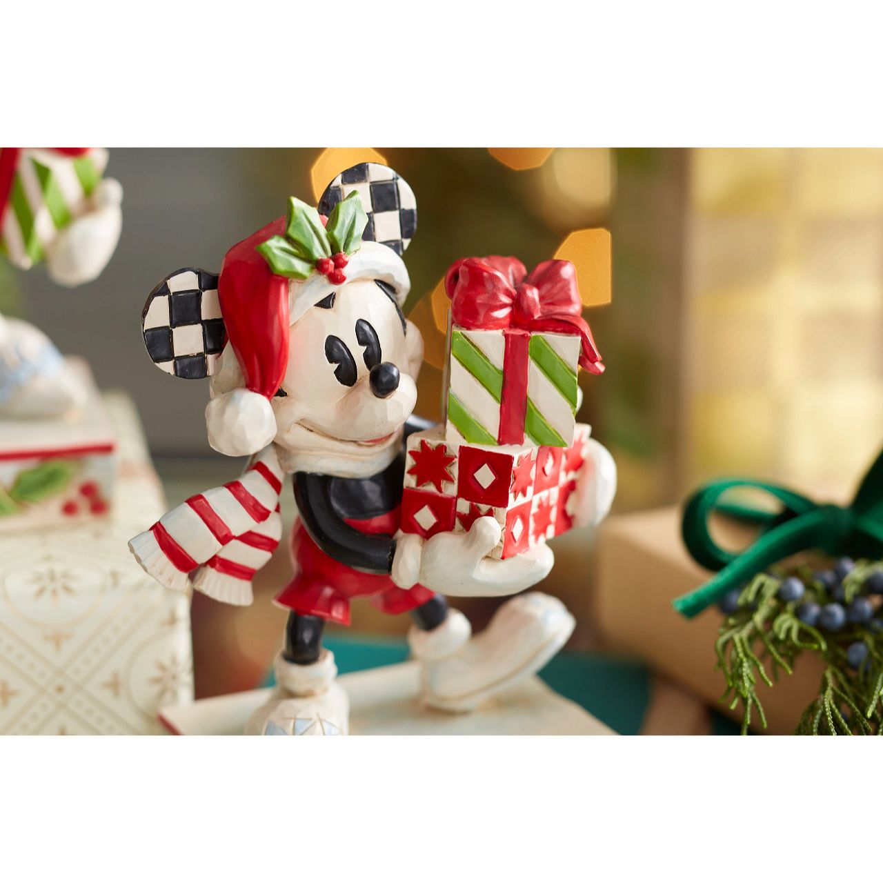 Jim Shore Christmas Mickey with Stack of Presents Figurine  Disney comes home for the holidays with this festive figurine by Jim Shore. Donning a candy cane striped scarf, Mickey wears a neighborly smile as he carries a towering stack of presents. The cheerful mouse boasts a holly brimmed Santa hat.