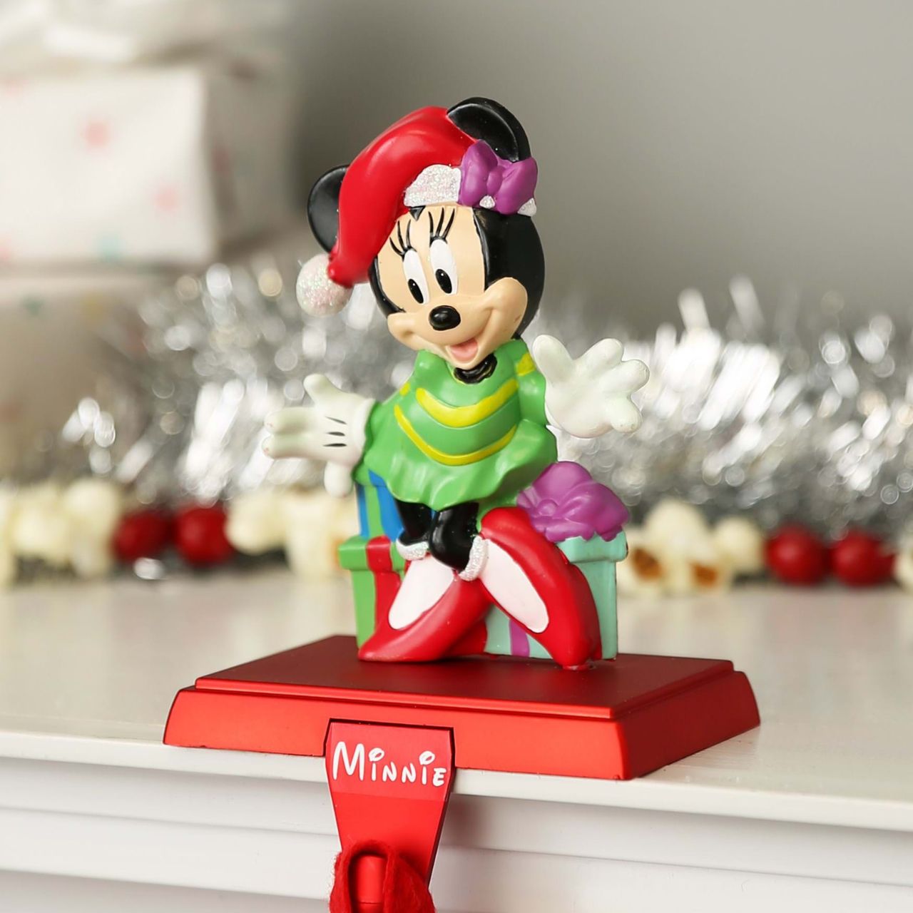 Kurt S Adler Minnie Mouse Stocking Holder  Hang up your favorite stocking this Christmas with this Disney Minnie Mouse stocking hanger from Kurt Adler. Features Minnie Mouse wearing a green dress, and a red and white Santa hat standing in front of wrapped presents.