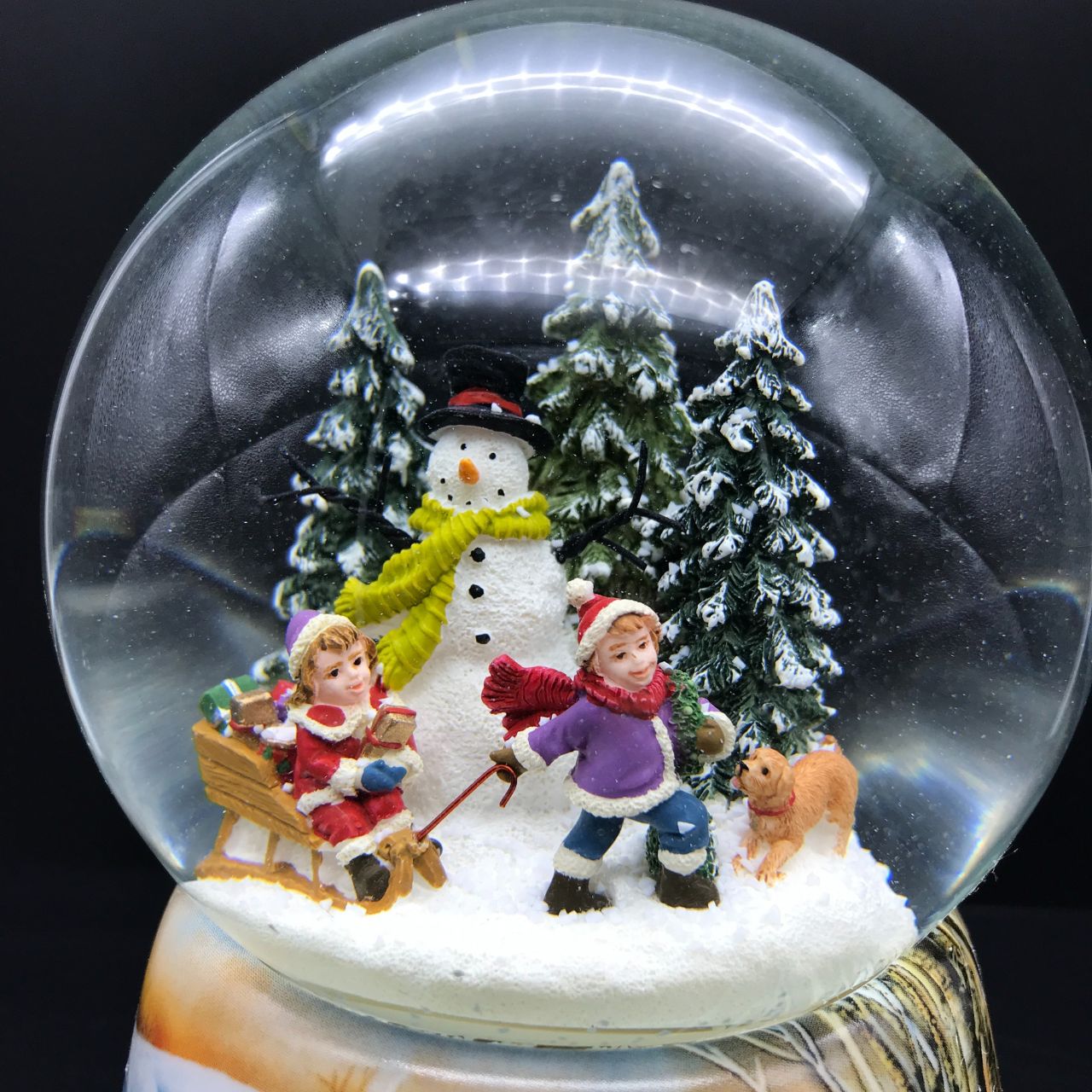 Music Box World Snow Globe Building a Snowman  Snow globe build a snowman. In the ball full of snow, two children with their sled pass by their snowman. Small snowy pine trees decorate the scene. The base is painted with snow-covered forest and village scenes.