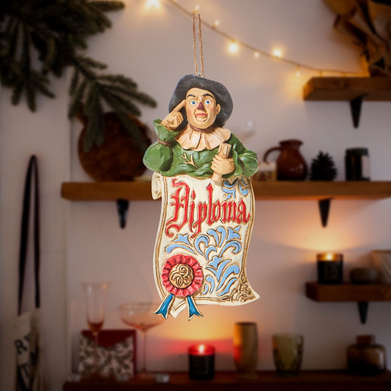 Jim Shore The Wizard of Oz Scarecrow Diploma Hanging Ornament  With a knowing tap to his head, an accomplished Scarecrow smiles from your tree. With a ribbon stamped diploma, it looks like this yellow brick road commuter finally got his wish this season. 